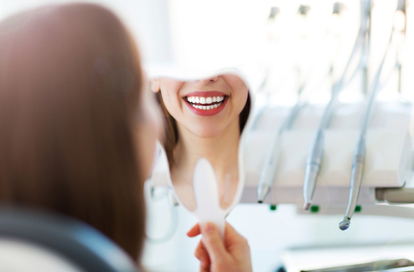 Woman looking at her smile in a mirror at Roane Family Dental in West Linn, OR